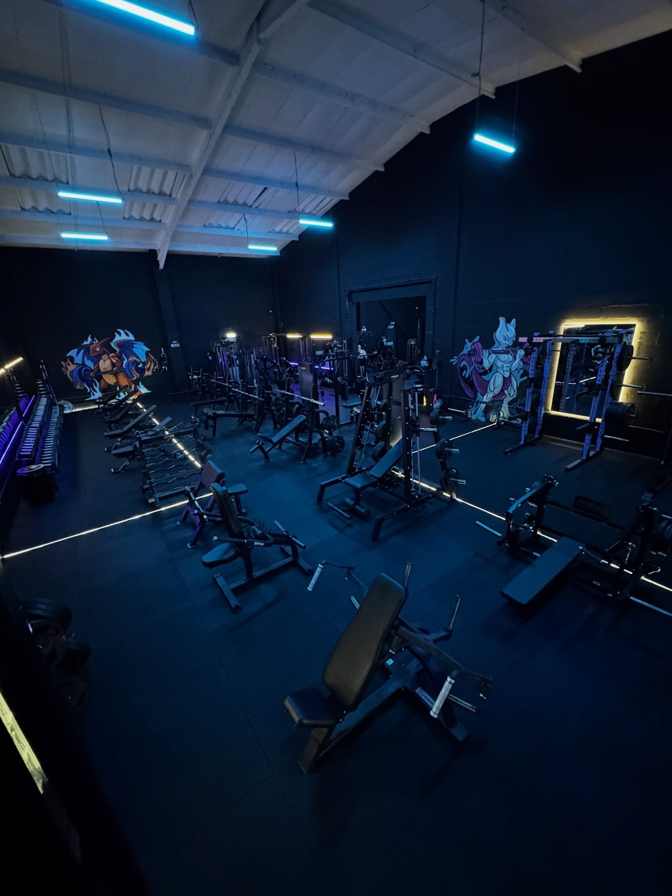 The gym floor at night, dark equipment lit by strips of blue LED light